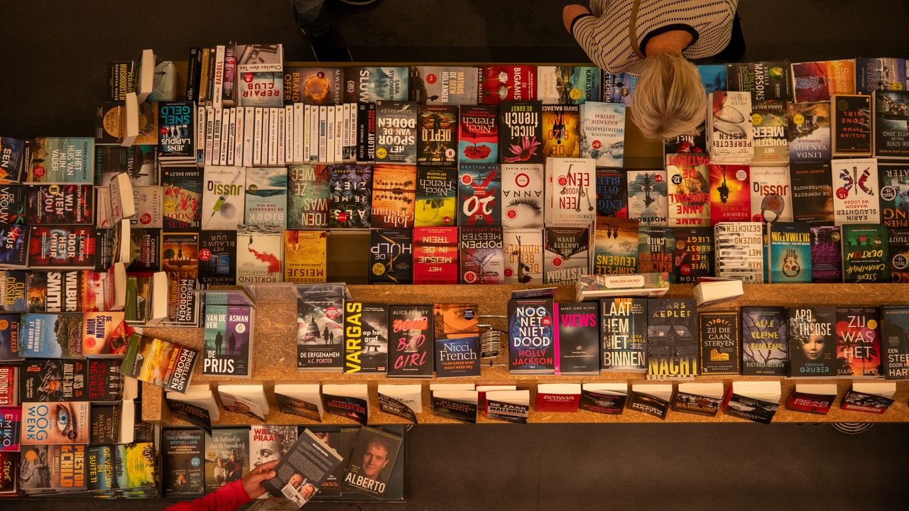 about-01 Overhead shot of a bookstore table filled with various books, with a customer browsing.