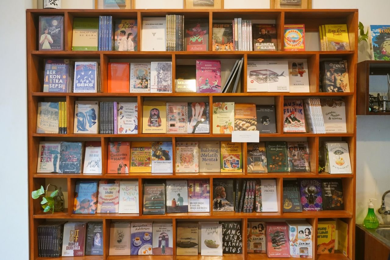 gallery-1 A vibrant display of books on a wooden shelf in a cozy bookstore, showcasing diverse literature.